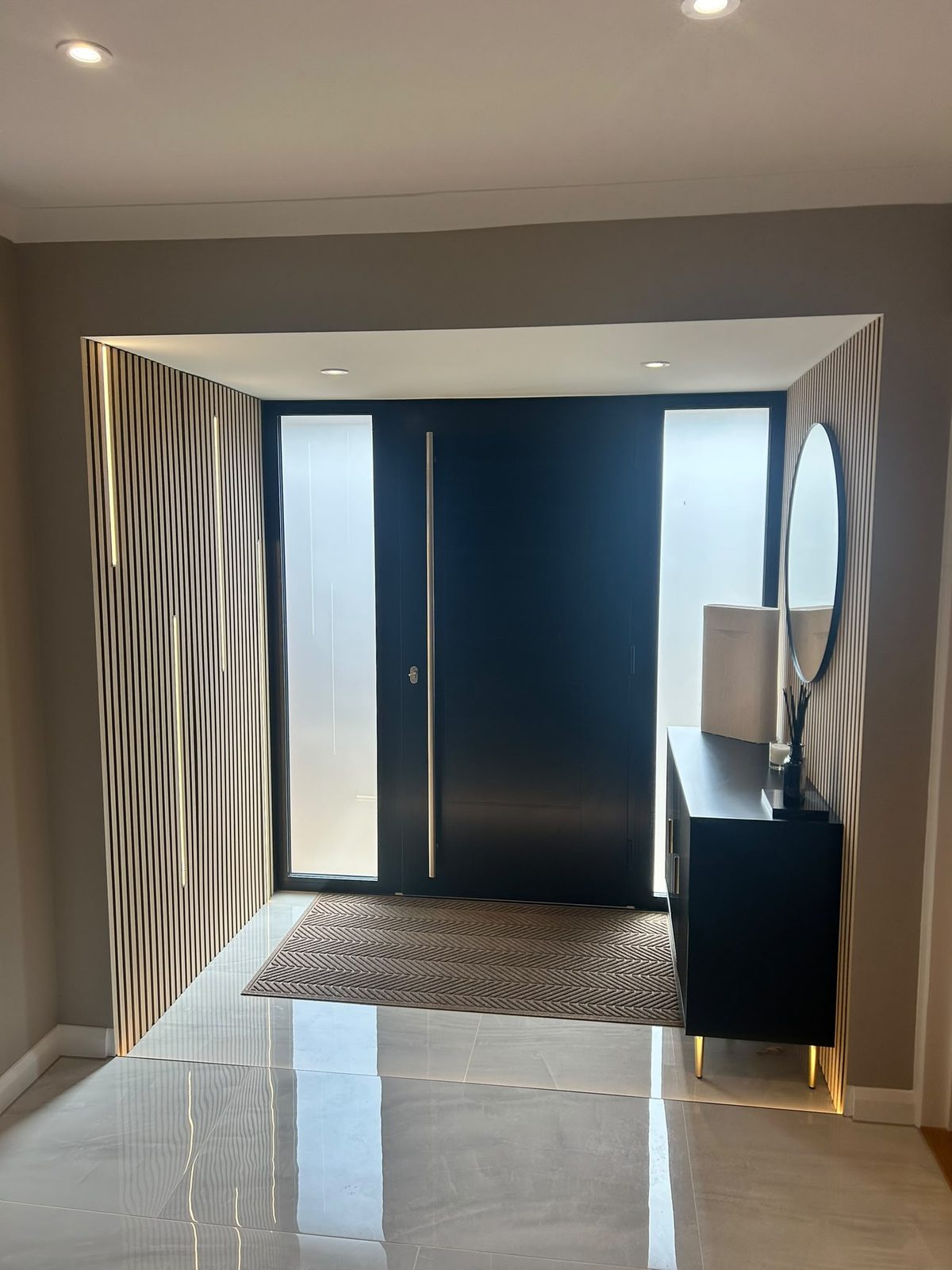 Dark front door with glazed side panel and slatted oak wall