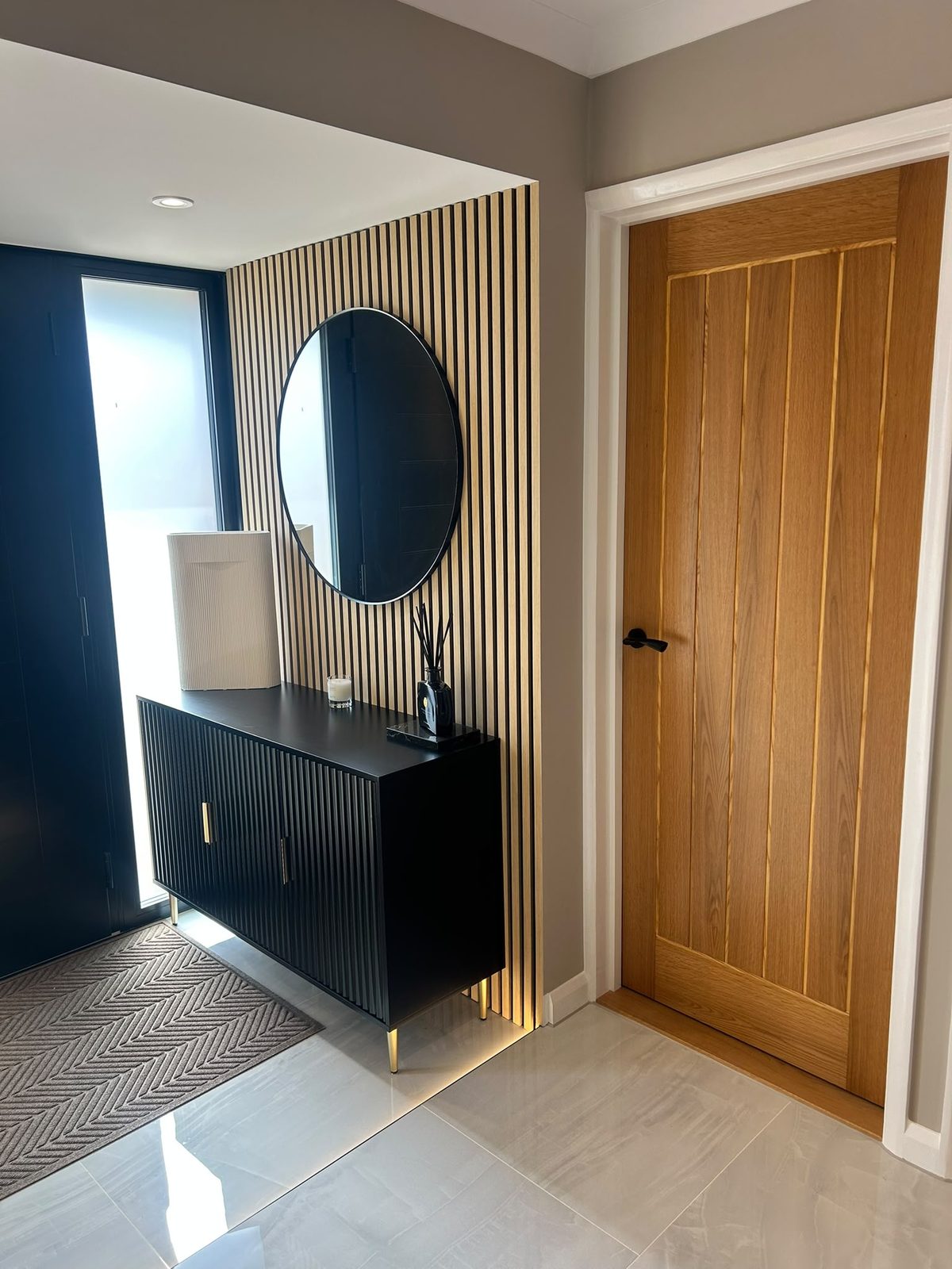 Slatted oak feature wall with round mirror and black console in the hallway