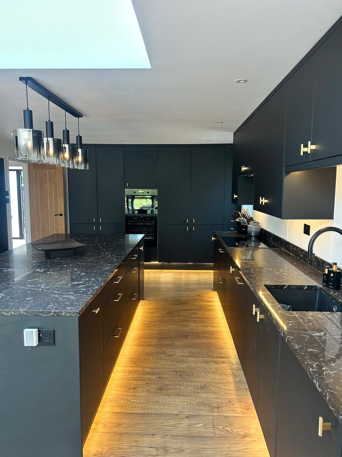 Black kitchen units with integrated ovens and stone splashback