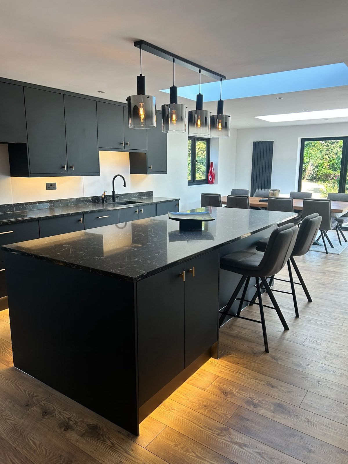 Matte black kitchen island with veined black stone worktop and smoked glass pendants