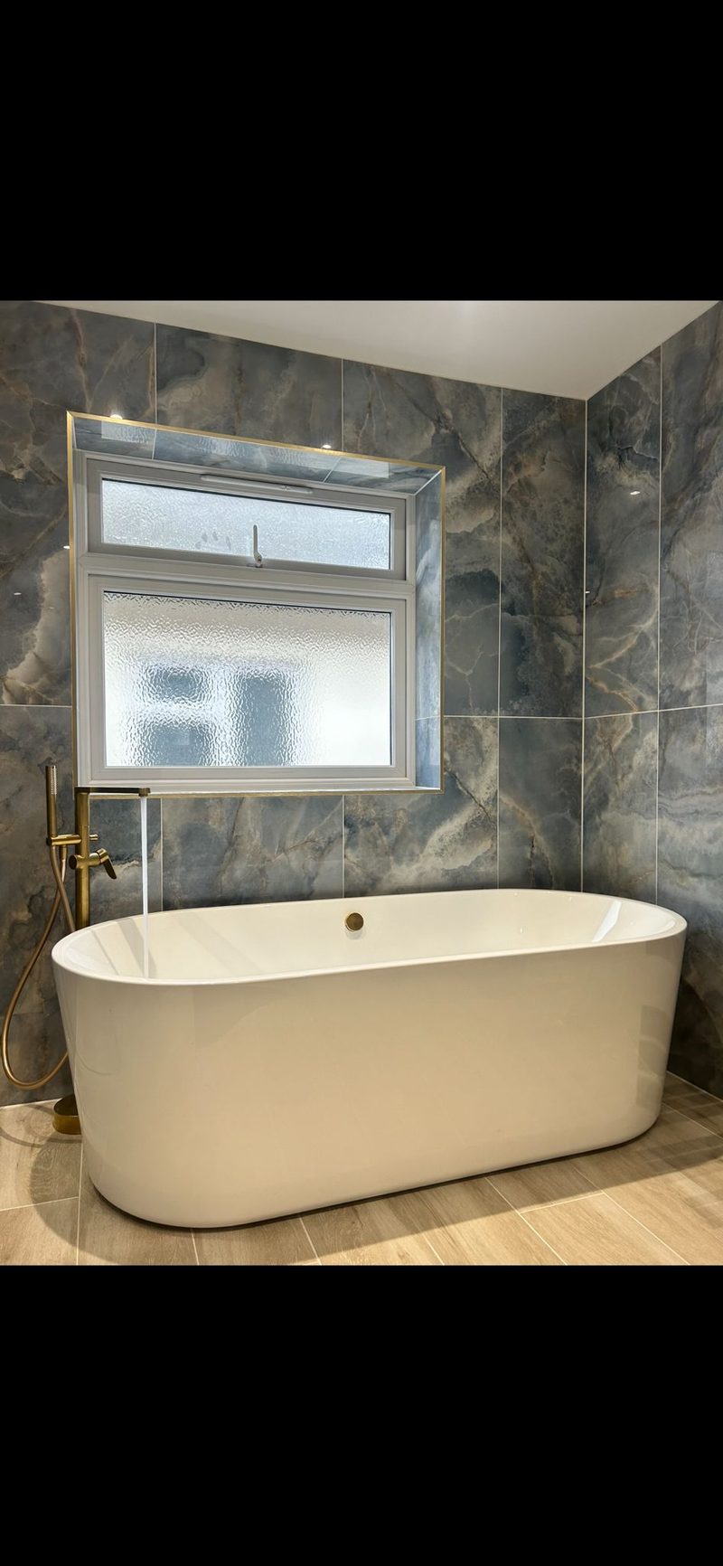 Freestanding bath with gold taps and marble tiles